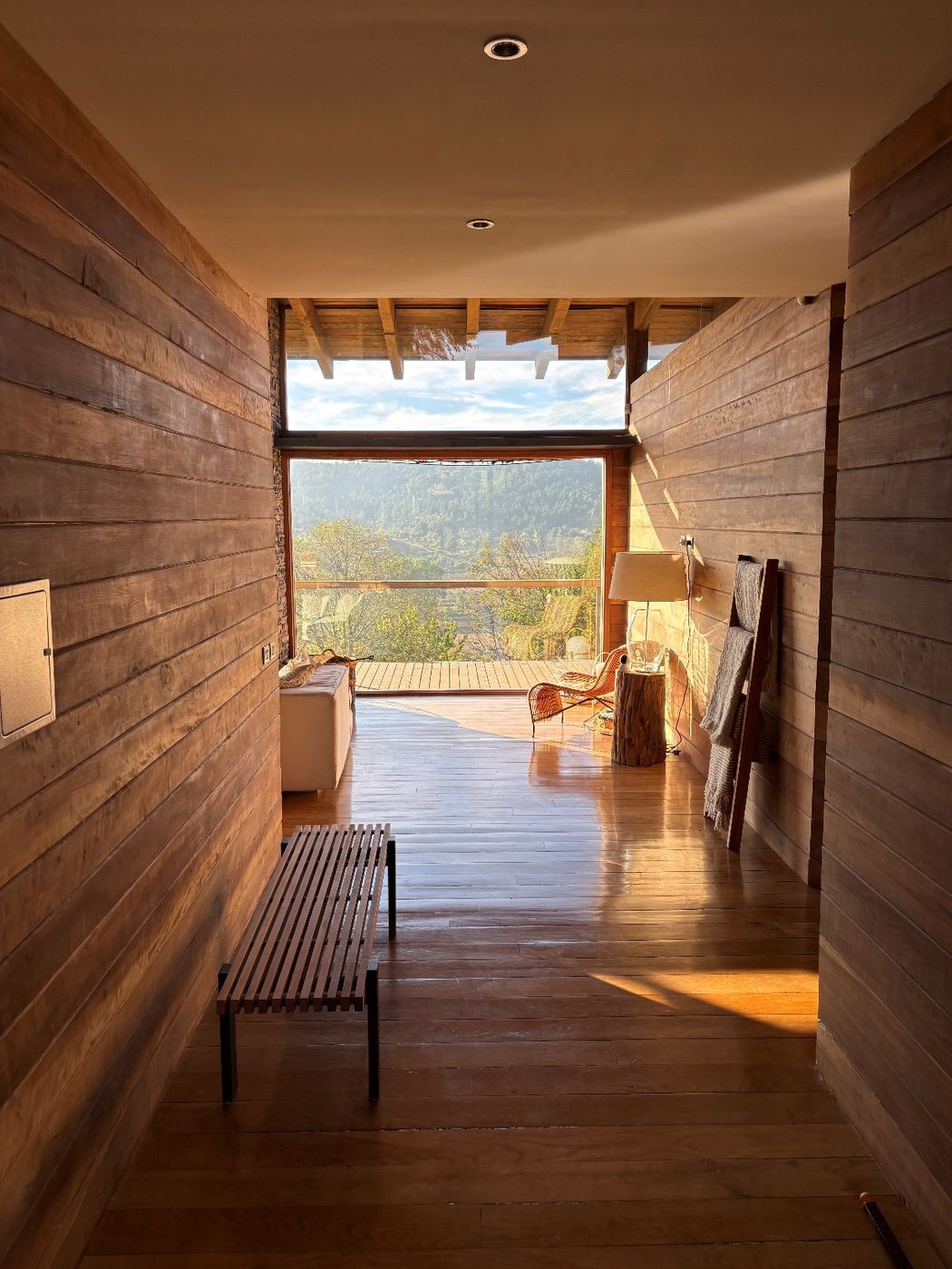 Pasillo de madera que remata en un ventanal con vista al paisaje del sur de Chile