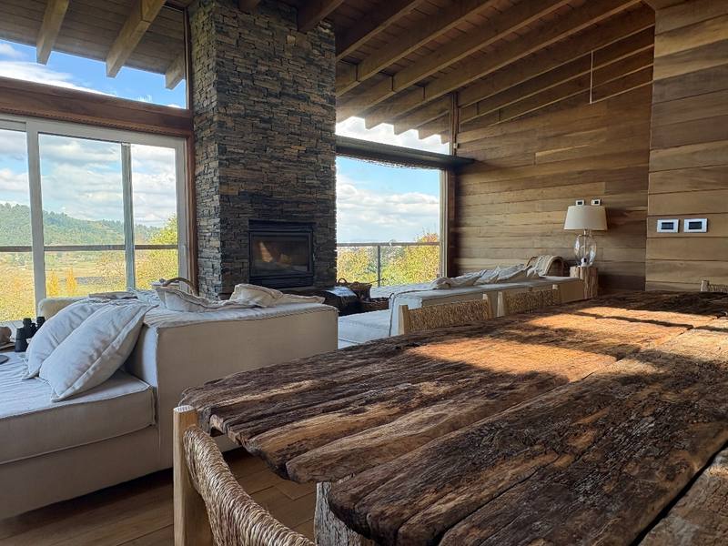 Casa Araucanía — Living con chimenea, mesa de madera rústica y vista al valle