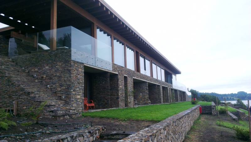 Lago Ranco I — Fachada de piedra con barandas de vidrio frente al lago