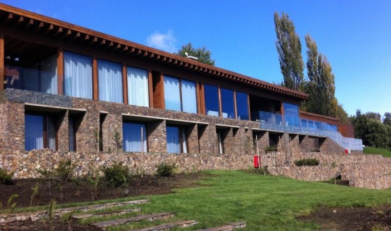 Lago Ranco I — Fachada de piedra y ventanales bajo cielo azul